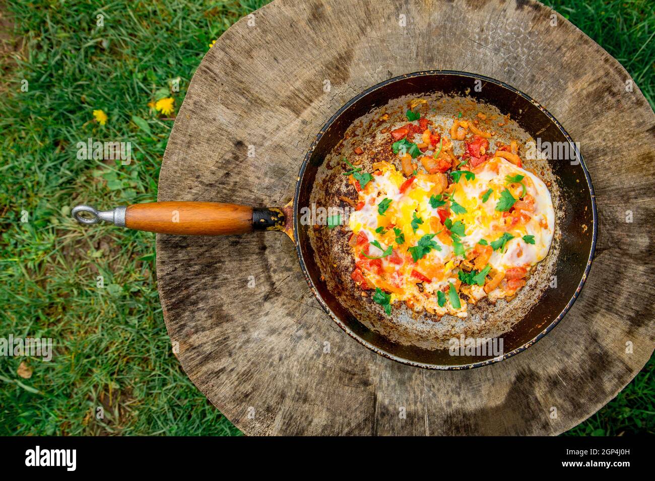 Gebratenes Omelett mit Eiern im Landhausstil mit Tomaten und Zwiebeln. Alte Bratpfanne mit Eiern auf Holzboden. Konzept - fetthaltige Lebensmittel, Adipositas Stockfoto