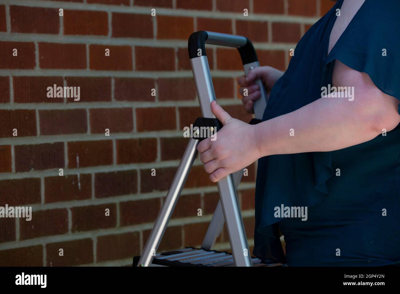 Frau, die eine Leiter in der Nähe eines roten Ziegels aufsetzt Wand Stockfoto