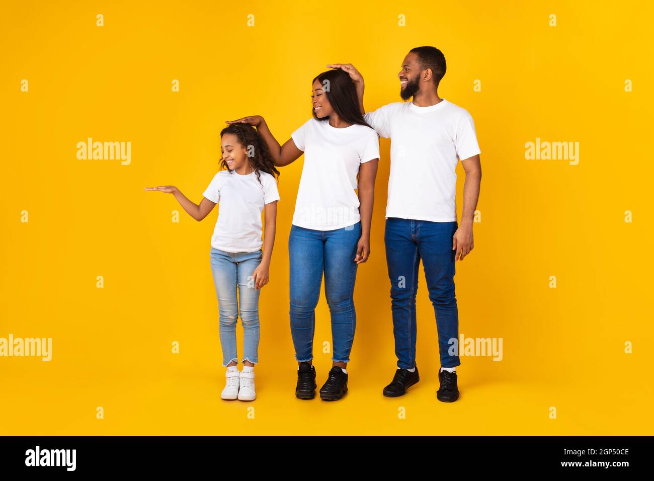 Foto in voller Körperlänge von drei Familienmitgliedern, die die Höhe mit der Handfläche messen. Lächelnde Mutter, Vater und Tochter, die sich bei der Entwicklung anfeuern Stockfoto