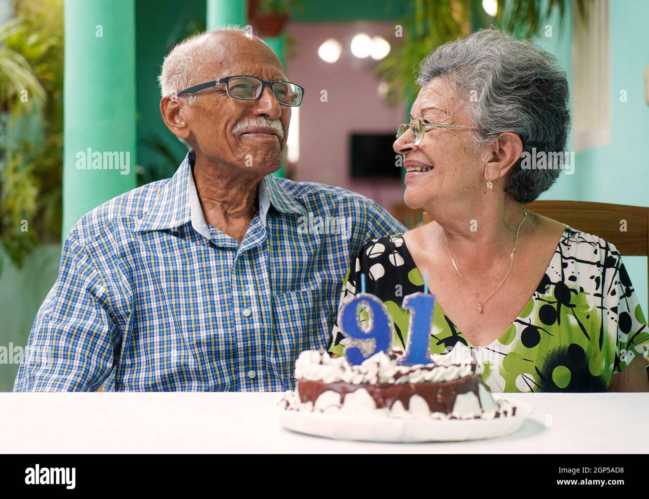 Ältere Paare mit einem Kuchen auf dem Tisch und die Nummer 91 auf dem Kuchen Stockfoto