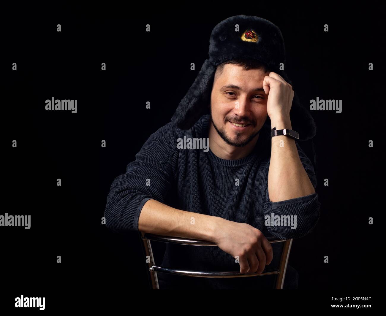 Porträt eines lächelnden Mannes von dreißig Jahren Kaukasischen Aussehen in einem sowjetischen Offiziersfell Hut auf einem schwarzen Hintergrund Stockfoto
