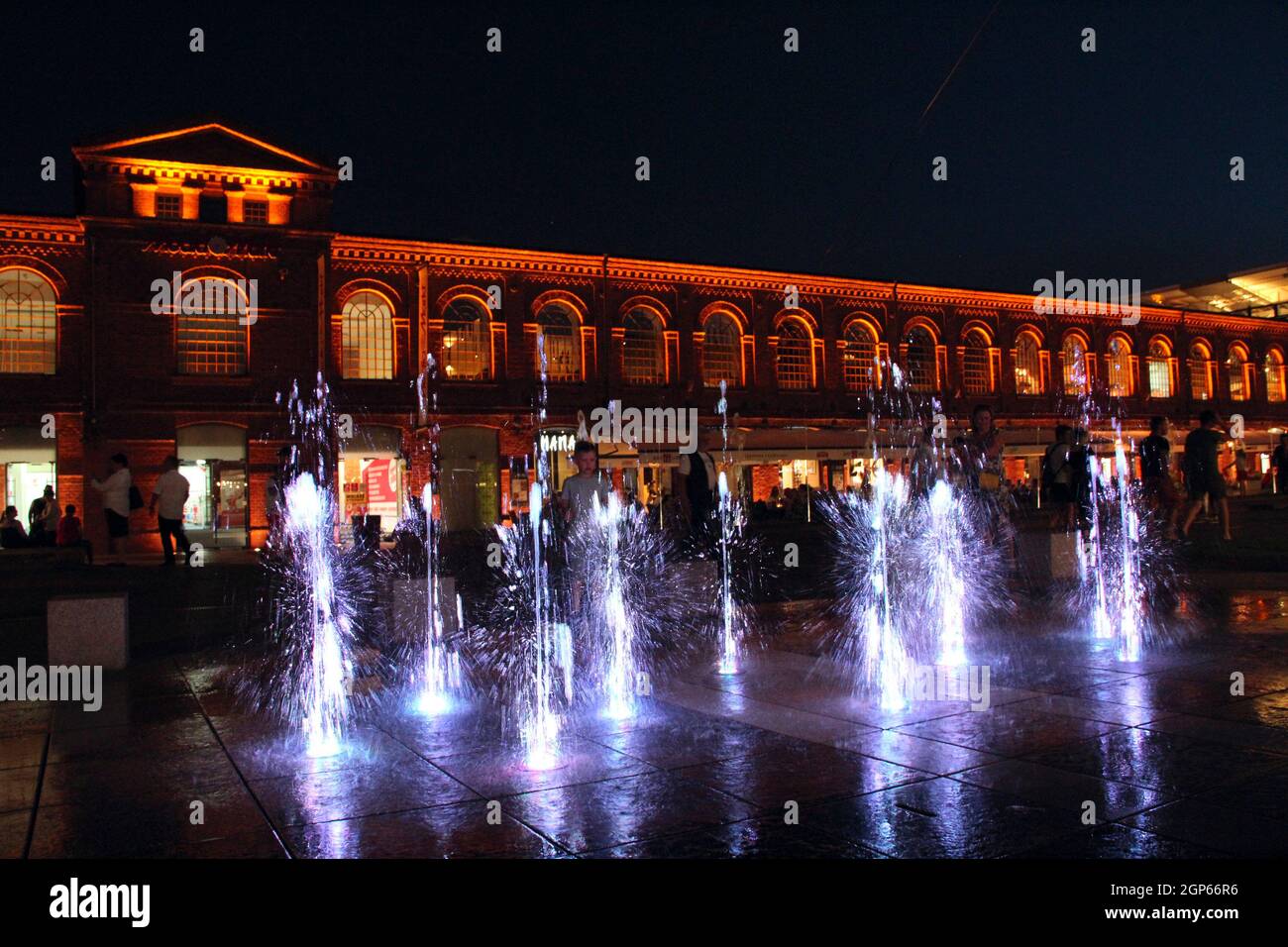 Kinder spielen mit Nachtbrunnen in der Stadt Lodz. Wunderschöne Abendbrunnen. Nachts erholen sich die Menschen in der Nähe von schönen beleuchteten Gebäuden. Stockfoto