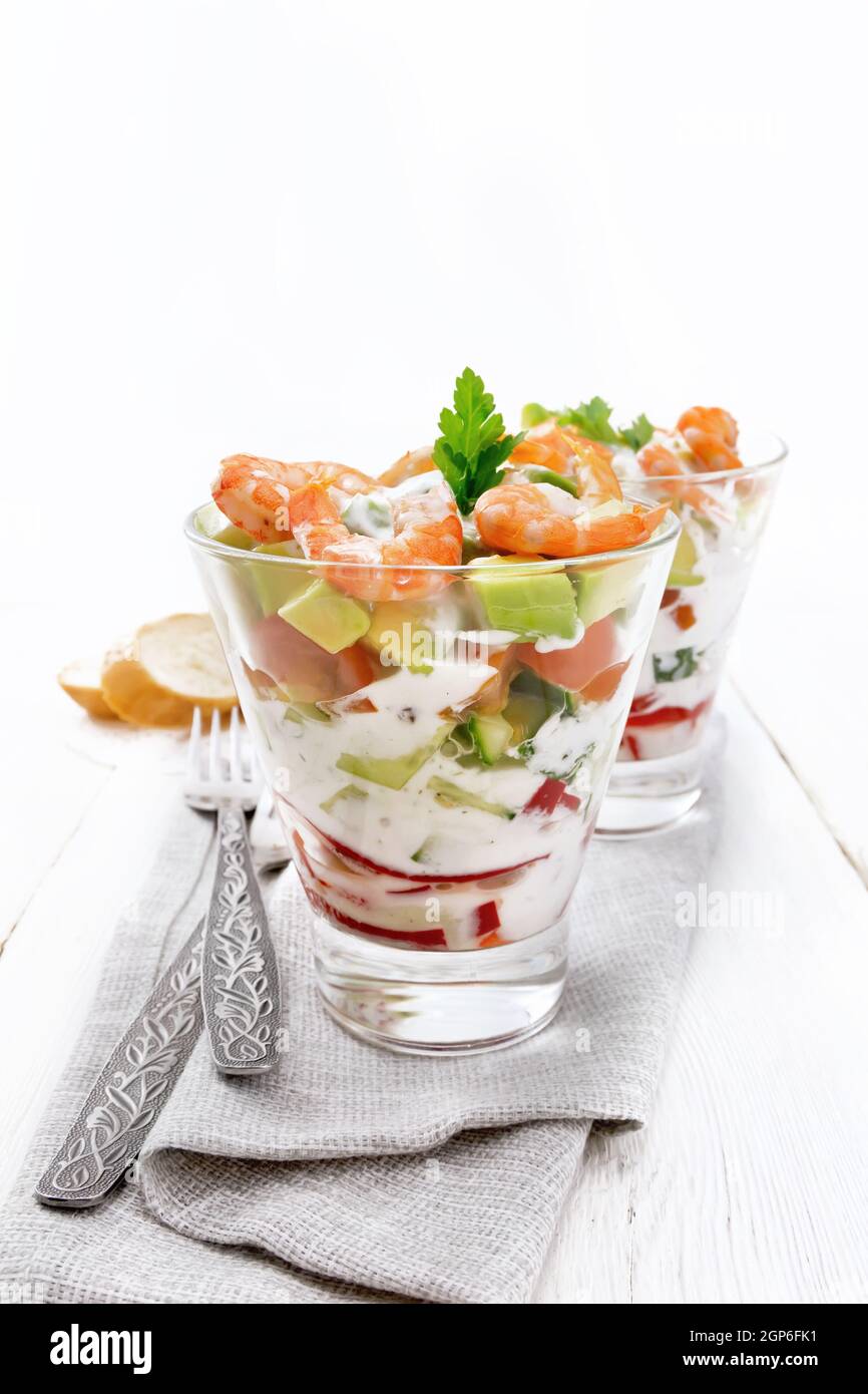 Puff Salat mit Garnelen, Avocado, frische Gurke, Paprika und Tomaten, gewürzt mit Joghurt Sauce in zwei Glas Gläser auf eine Serviette, Brot und Gabeln Stockfoto