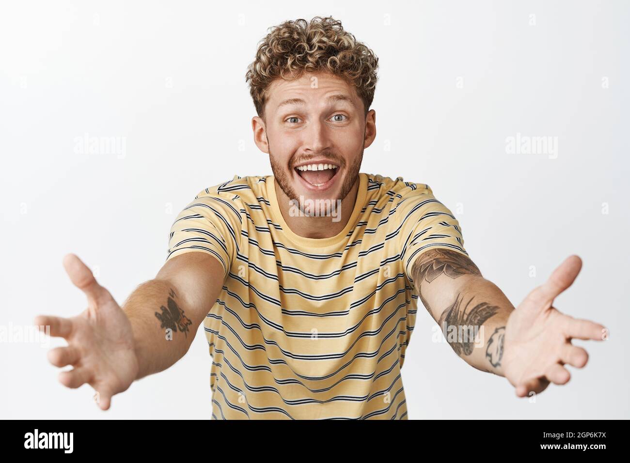 Glücklicher junger Mann, der die Hände streckt, um jemanden zu halten, auf Umarmung wartet, etwas in seinen Armen empfängt und auf weißem Hintergrund steht Stockfoto