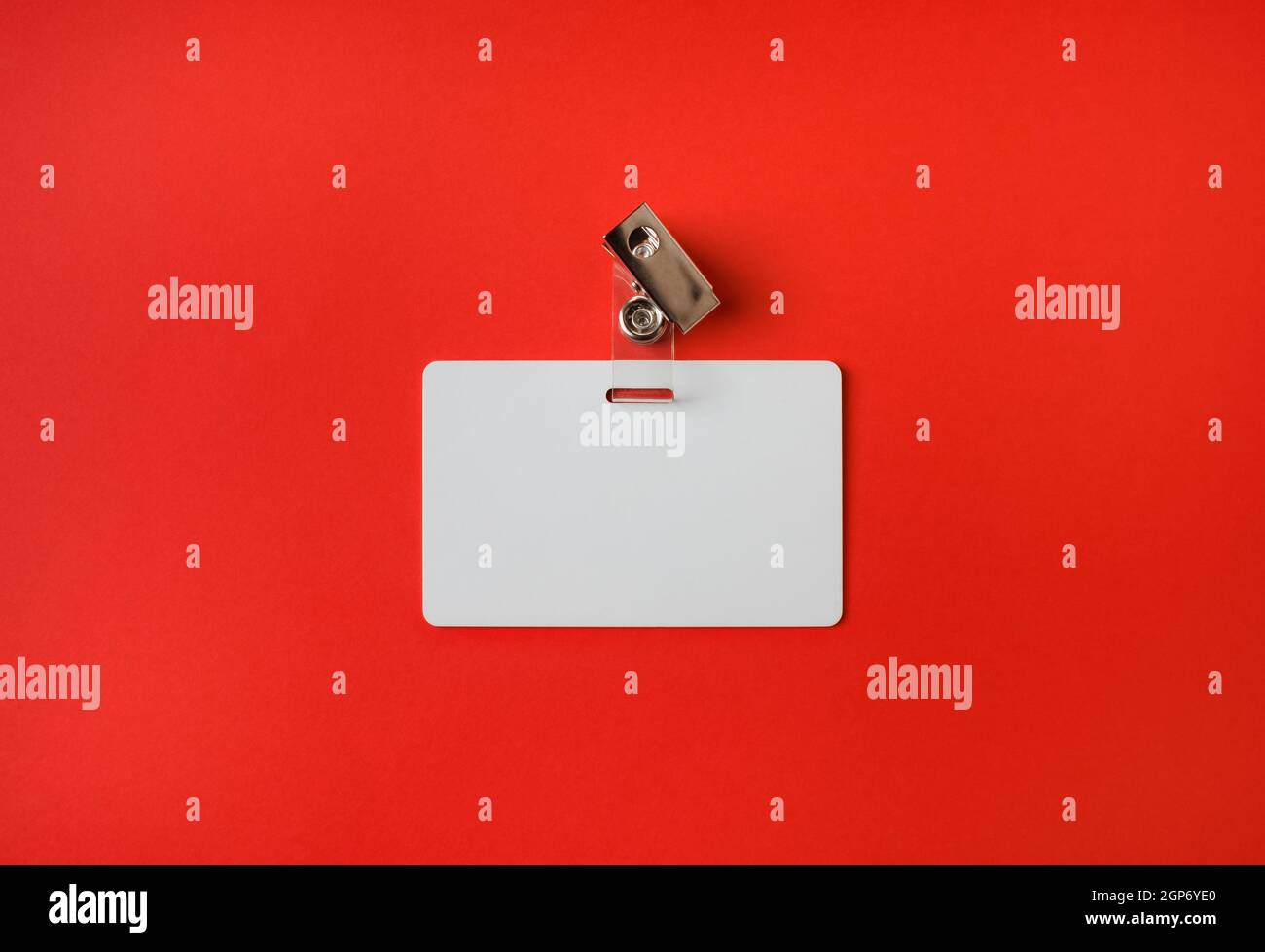 Foto des weißen Plastikabzeichens auf rotem Papierhintergrund. Leerer personalausweis. Draufsicht. Flach liegend. Stockfoto