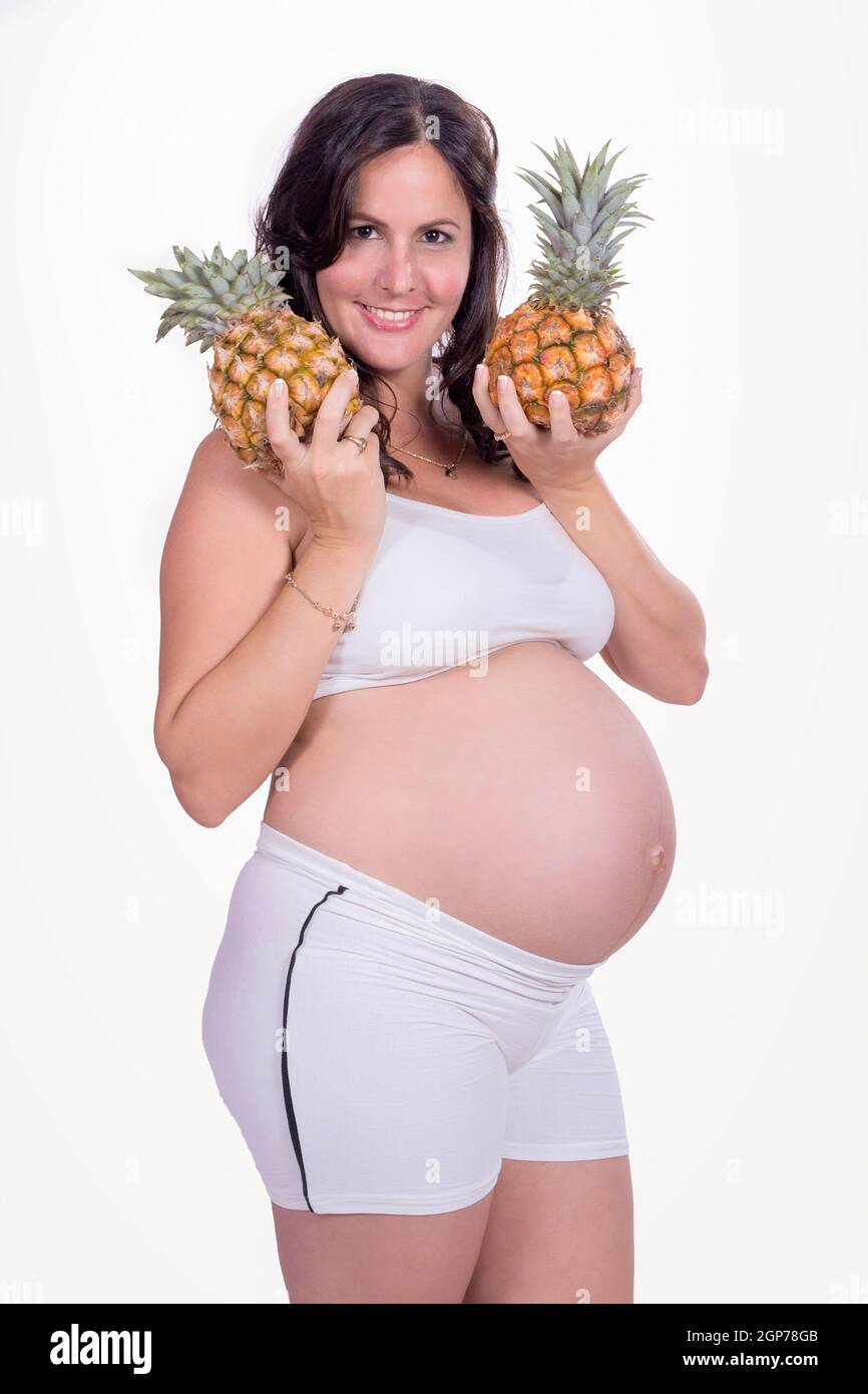 Eine schwangere Frau mit Ananas in ihren Händen, weiße Kleidung zu tragen. Stockfoto