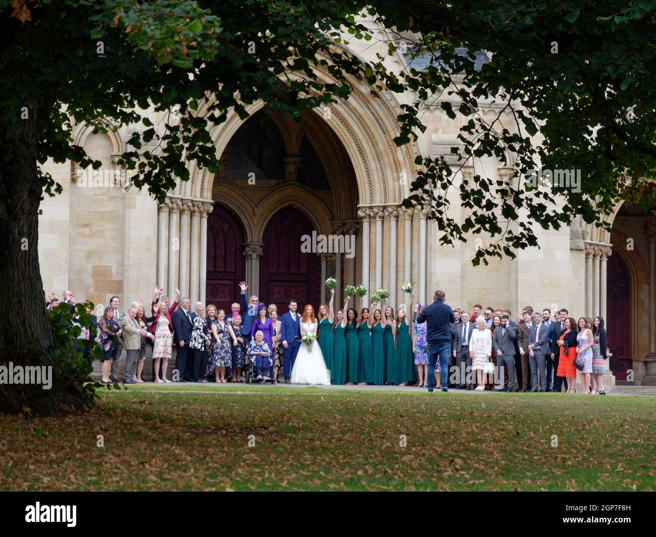 St Albans, Hertfordshire, England, September 21 2021: Herbstliche Hochzeit vor der Kathedrale, während die Brautjungfern Blumensträuße für ein Pho in der Luft halten Stockfoto
