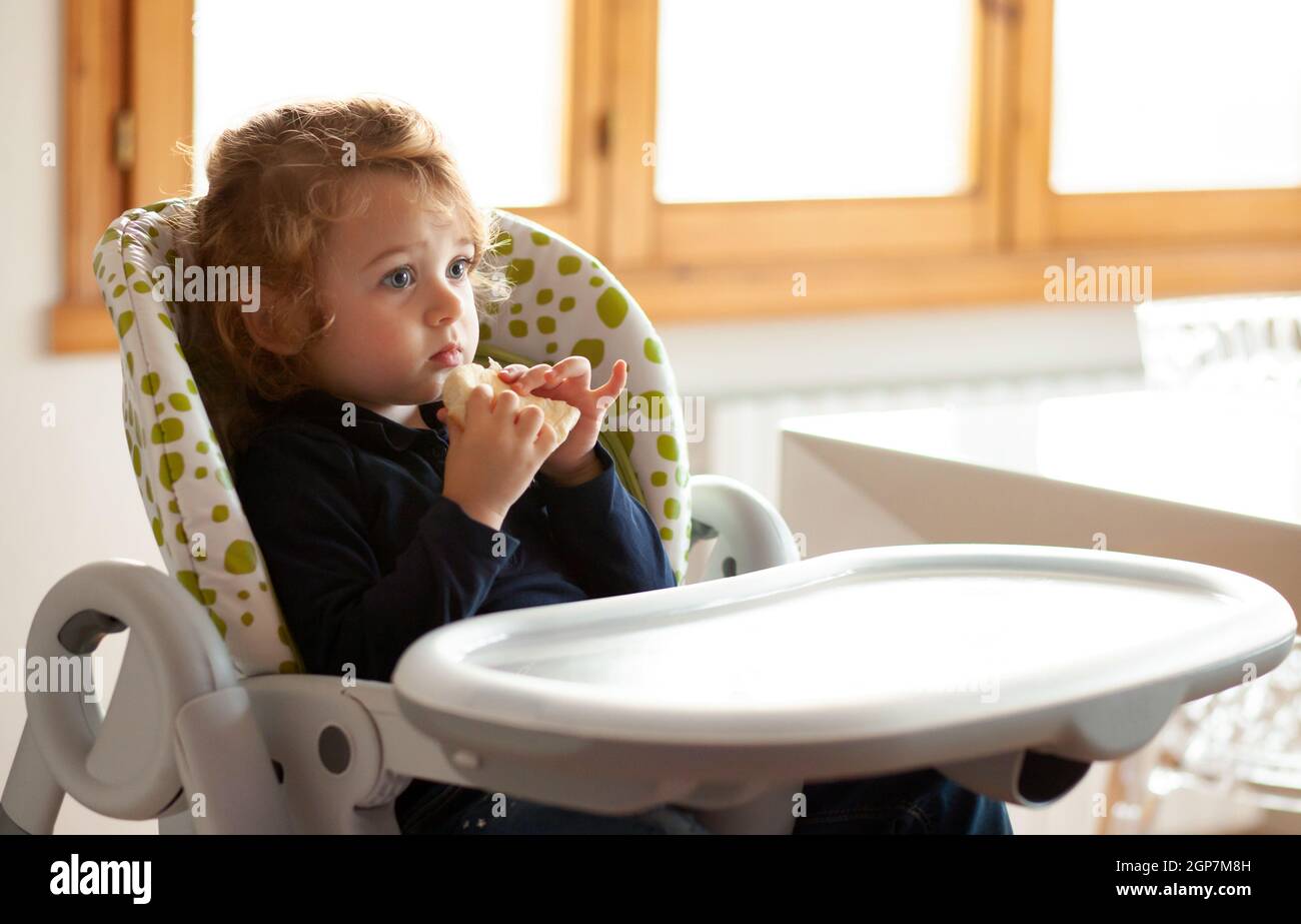 Kleines Mädchen isst Brot in den Hochstuhl. Stockfoto