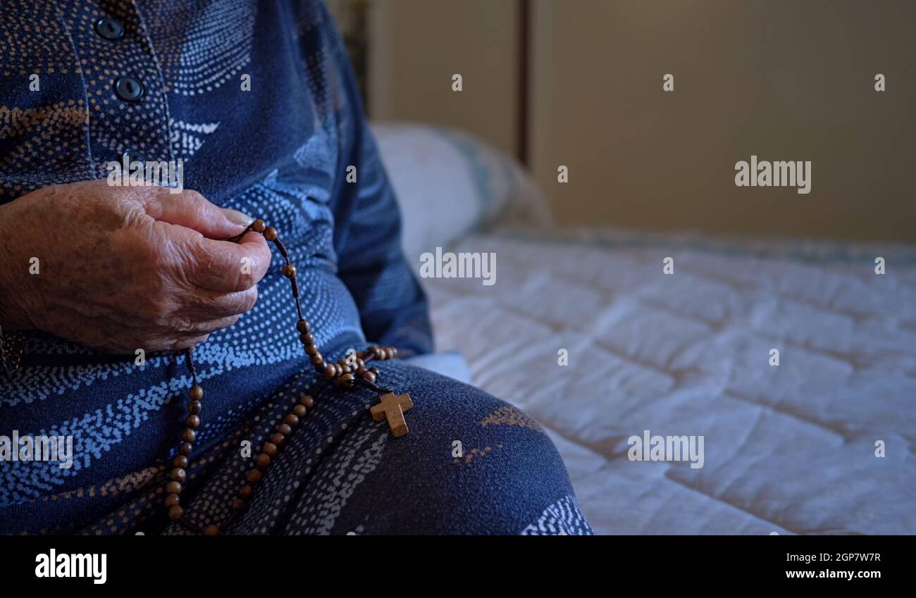 Ältere Frau 70-80 Jahre alt betet mit dem Rosenkranz zu Hause. Stockfoto