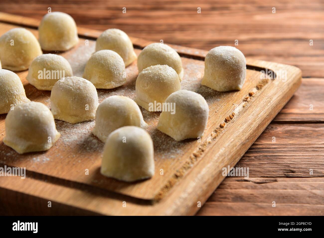 Gefrorene hausgemachte Rohkost von Ravioli auf Holzbretttisch, Kochvorgang halbfertige Pelmeni Knödel. Stockfoto