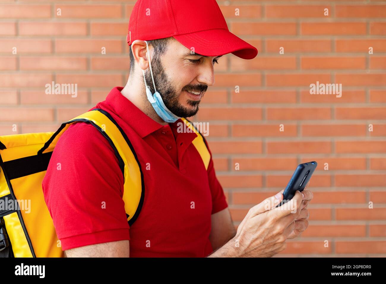 Delivery man in Gesichtsmaske mit Handy, während der Lieferung von Paketen Stockfoto
