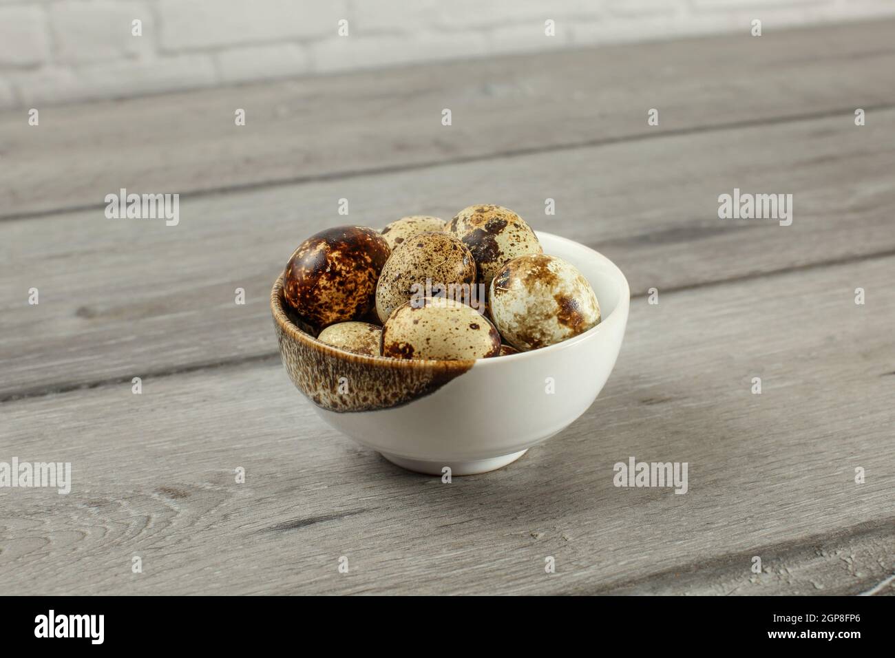 Gefleckte Wachteleier in kleinen Porzellan Schüssel auf grau Holzschreibtisch. Stockfoto