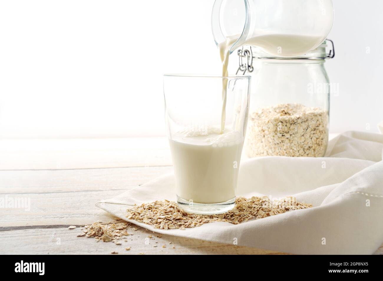 Vegane Hafermilch wird in ein Trinkglas gegossen, gesunde, nicht milchige Alternative auf einem hellen Holztisch, Kopierraum, ausgewählter Fokus, enge Fie-Tiefe Stockfoto