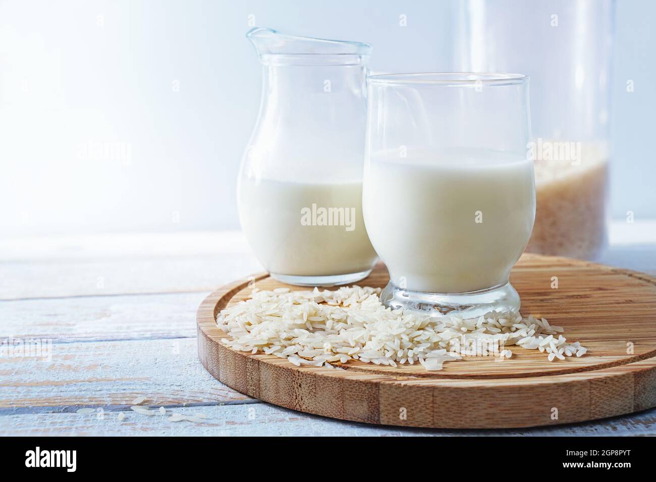 Vegane Reismilch, gesunde Alternative ohne tierische Milchprodukte in einem Trinkglas und einem Krug auf einem hölzernen Küchbrett vor hellem Hintergrund, Stockfoto