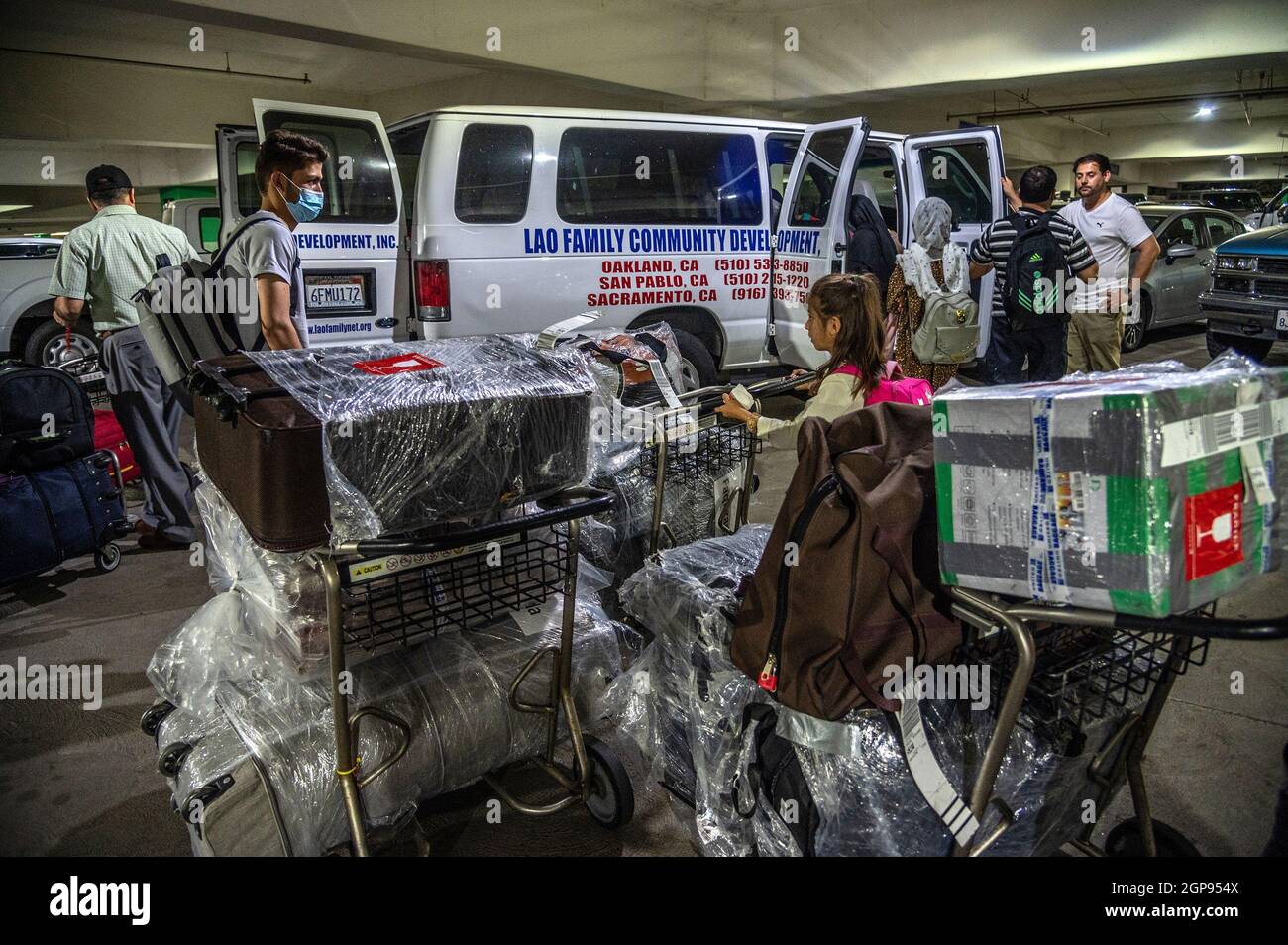 Sacramento, Kalifornien, USA. August 2021. Mit den Besitztümern, die seine Familie auf Karren aus Afghanistan gebracht hatte, plaudert ABDUL mit NAIMANTULLAH SULTANI, ganz rechts, von der Umsiedlungsagentur Lao Family Community Development, die die Familie am internationalen Flughafen von Sacramento abgeholt hat. Sultani kam 2019 mit einem Visa für besondere Einwanderer aus Afghanistan in die USA. (Bild: © Renee C. Byer/Sacramento Bee/ZUMA Press Wire) Stockfoto