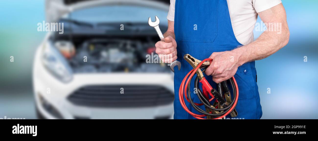 Kfz-Mechaniker hält Sprungleitungen und Schlüssel auf Werkstatt Hintergrund Stockfoto