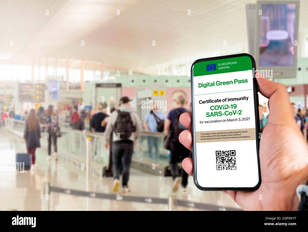 Der digitale grüne Pass der europäischen Union mit dem QR-Code auf dem Bildschirm eines Handys an einer Hand gehalten mit verschwommenem Flughafen im Hintergrund. Immunit Stockfoto