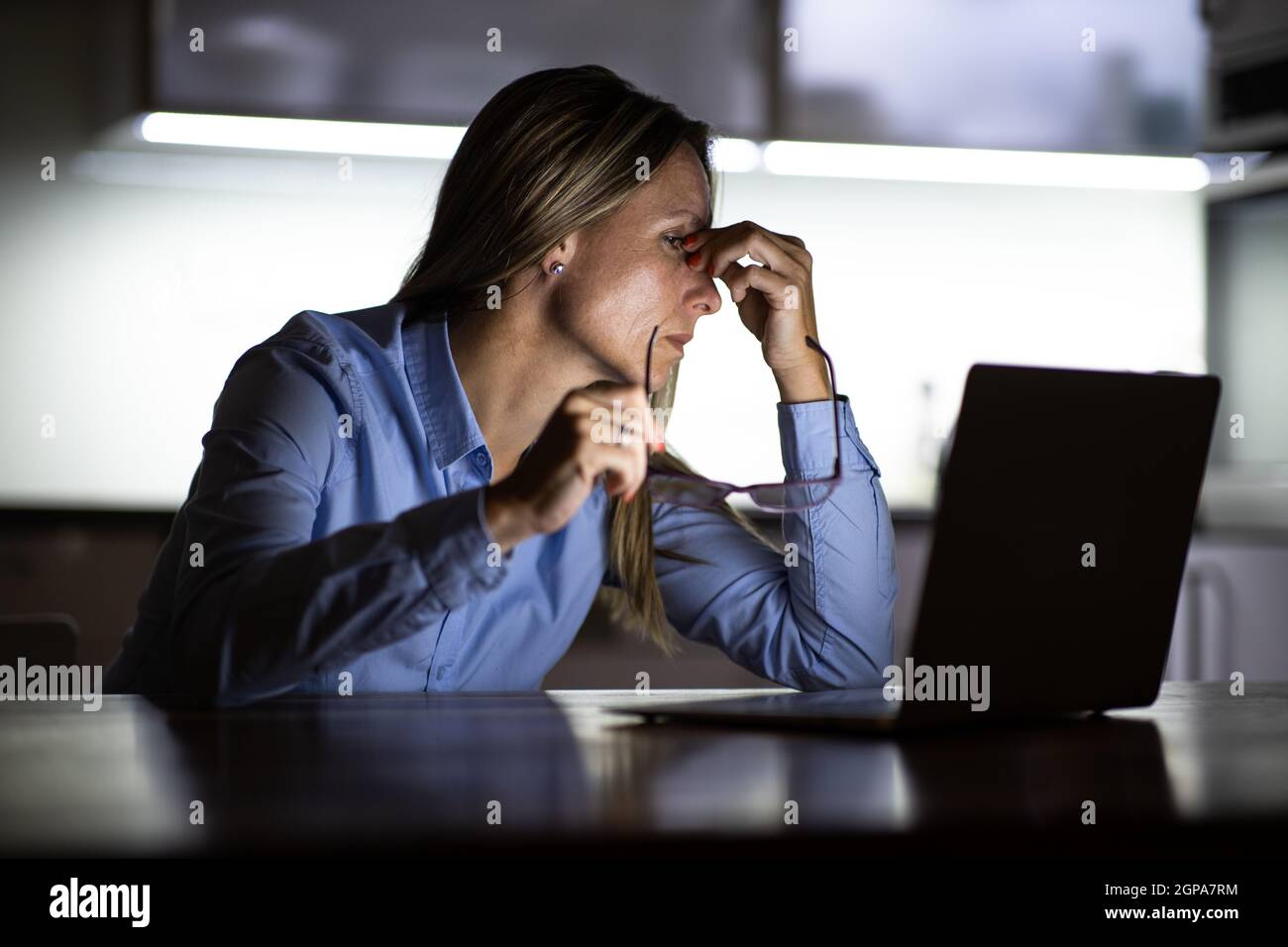 Hübsche Frau mittleren Alters, die spät am Tag auf einem Laptop-Computer zu Hause arbeitet, ein Geschäft von zu Hause aus führt, aus der Ferne arbeitet - frustriert wird, e Stockfoto