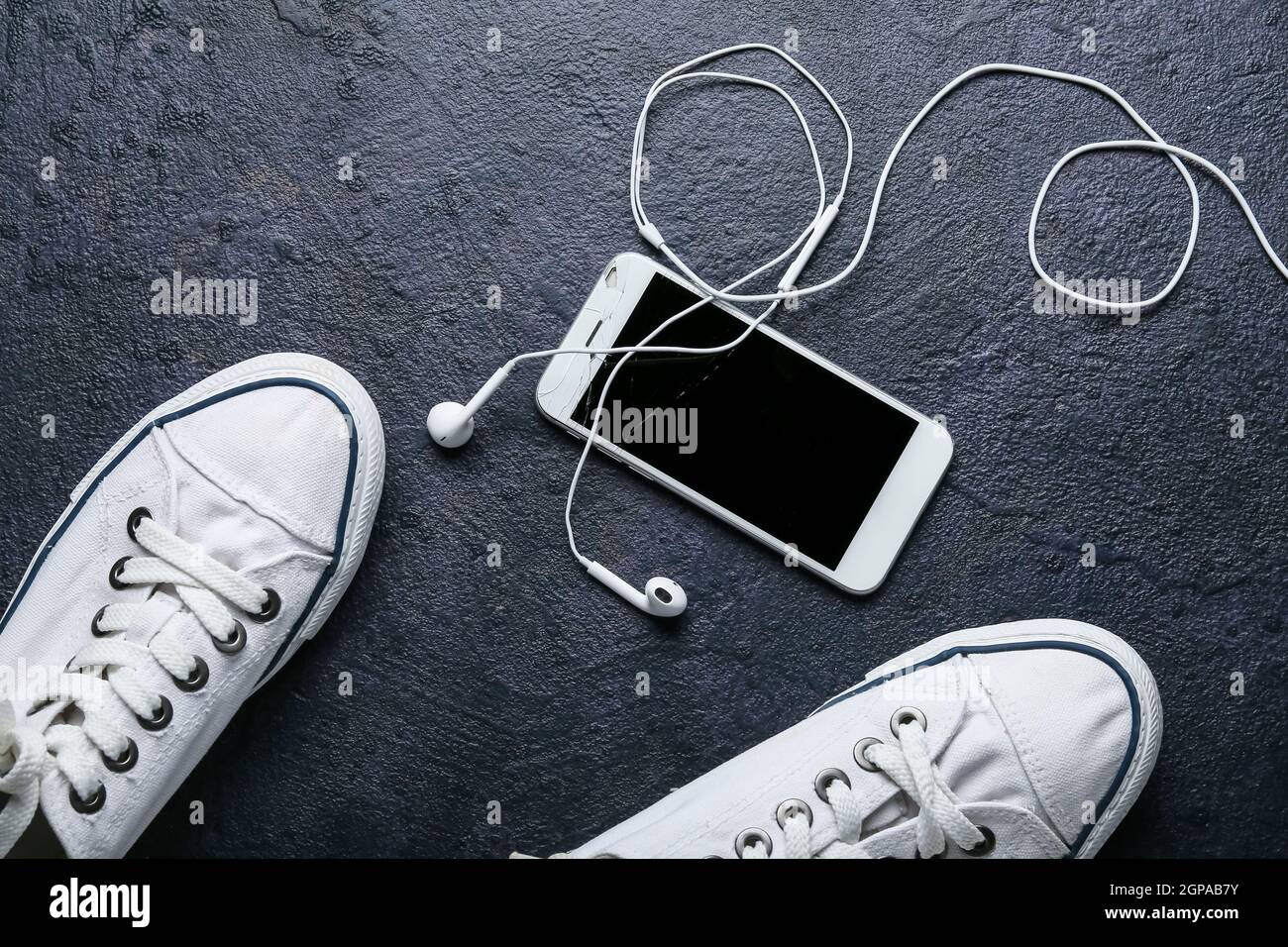 Handy mit kaputten Bildschirm, Kopfhörer und Schuhe auf dunklem Hintergrund  Stockfotografie - Alamy