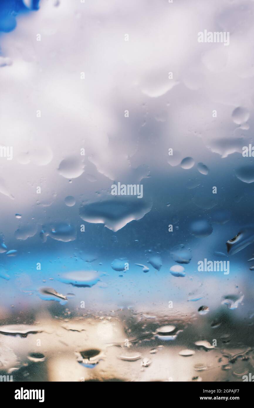 Selektiver Fokus von Regentropfen auf einer Glasfensterfläche mit wunderschönem verschwommenem Himmel und Wolken im Hintergrund. Dramatisches Hintergrundkonzept. Leicht nach hinten Stockfoto