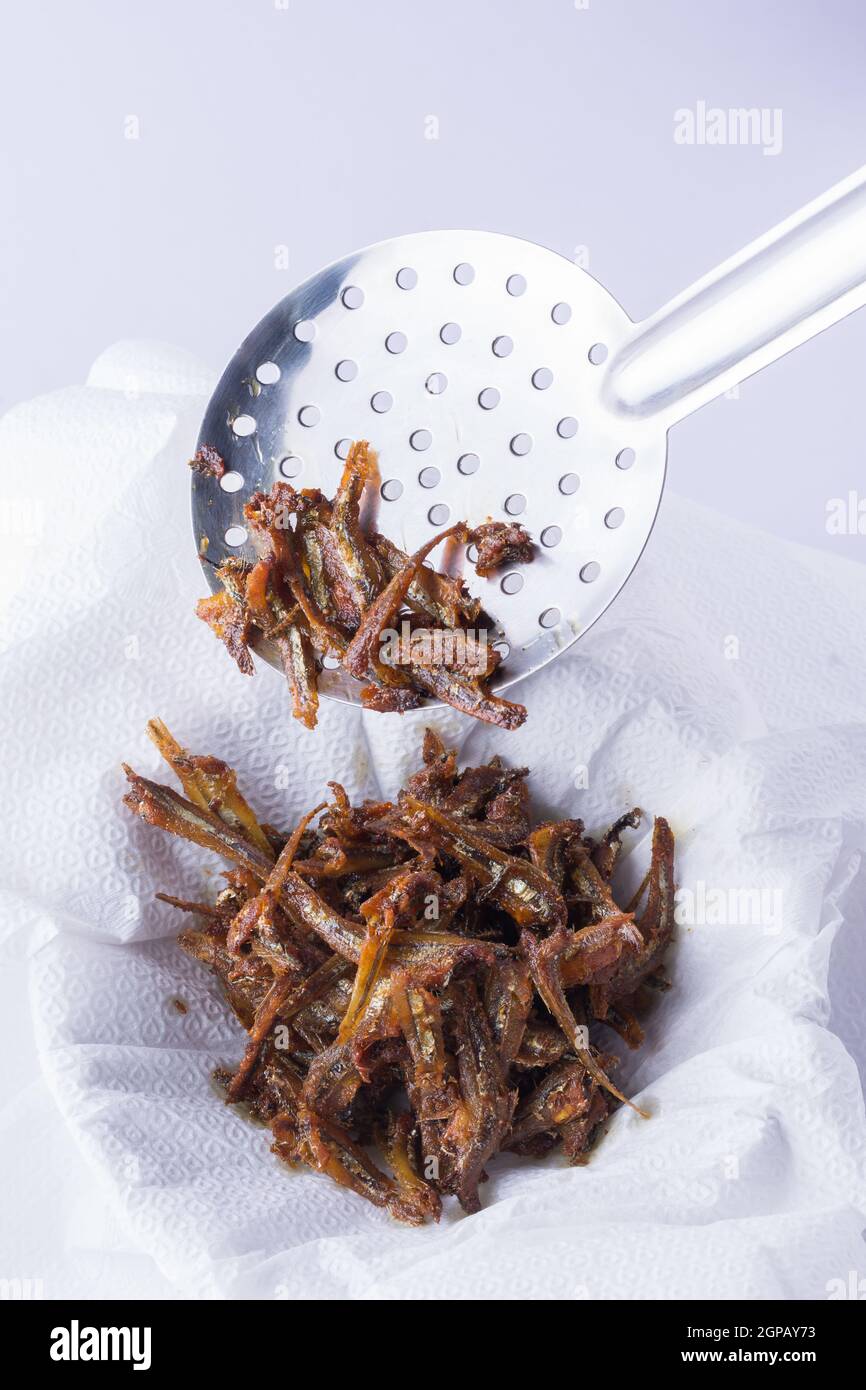 Frittierter kleiner trockener Fisch, knusprige frittierte Meeresfrüchte bereit zum Servieren auf weißem Hintergrund, Öl auf einem lebensmittelsicheren Papiertuch abtropfen lassen Stockfoto