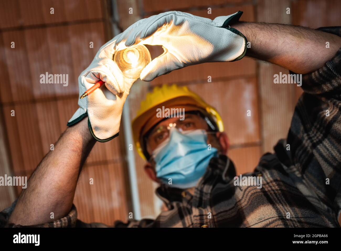 Elektriker Arbeiter bei der Arbeit ersetzt die Glühbirne durch Helm, Schutzbrille und Handschuhe geschützt; tragen Sie die OP-Maske, um die Ausbreitung von COR zu verhindern Stockfoto