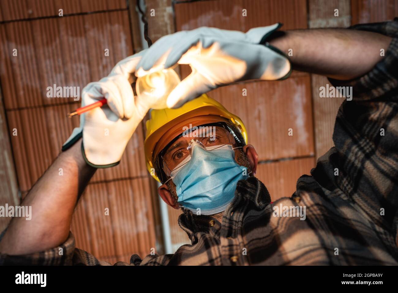 Elektriker Arbeiter bei der Arbeit ersetzt die Glühbirne durch Helm, Schutzbrille und Handschuhe geschützt; tragen Sie die OP-Maske, um die Ausbreitung von COR zu verhindern Stockfoto