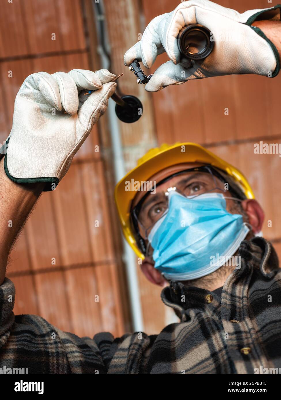 Elektriker Arbeiter bei der Arbeit ersetzt die Lampenfassung durch Helm, Schutzbrille und Handschuhe geschützt; tragen Sie die OP-Maske, um die Ausbreitung von Co zu verhindern Stockfoto