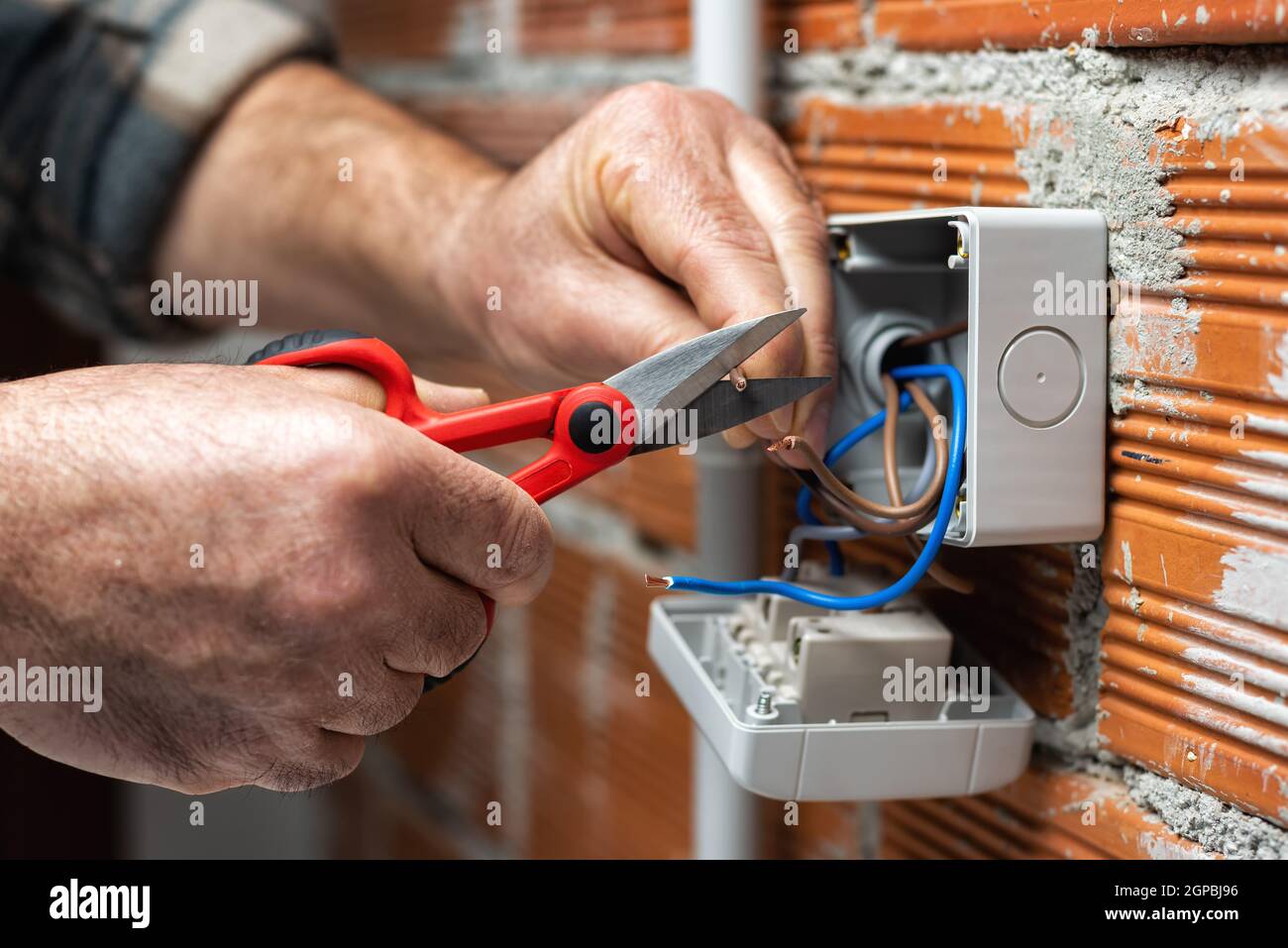 Der Elektriker Arbeiter bei der Arbeit mit der Schere bereitet die elektrischen Kabel des häuslichen elektrischen Systems vor. Bauindustrie. Stockfoto