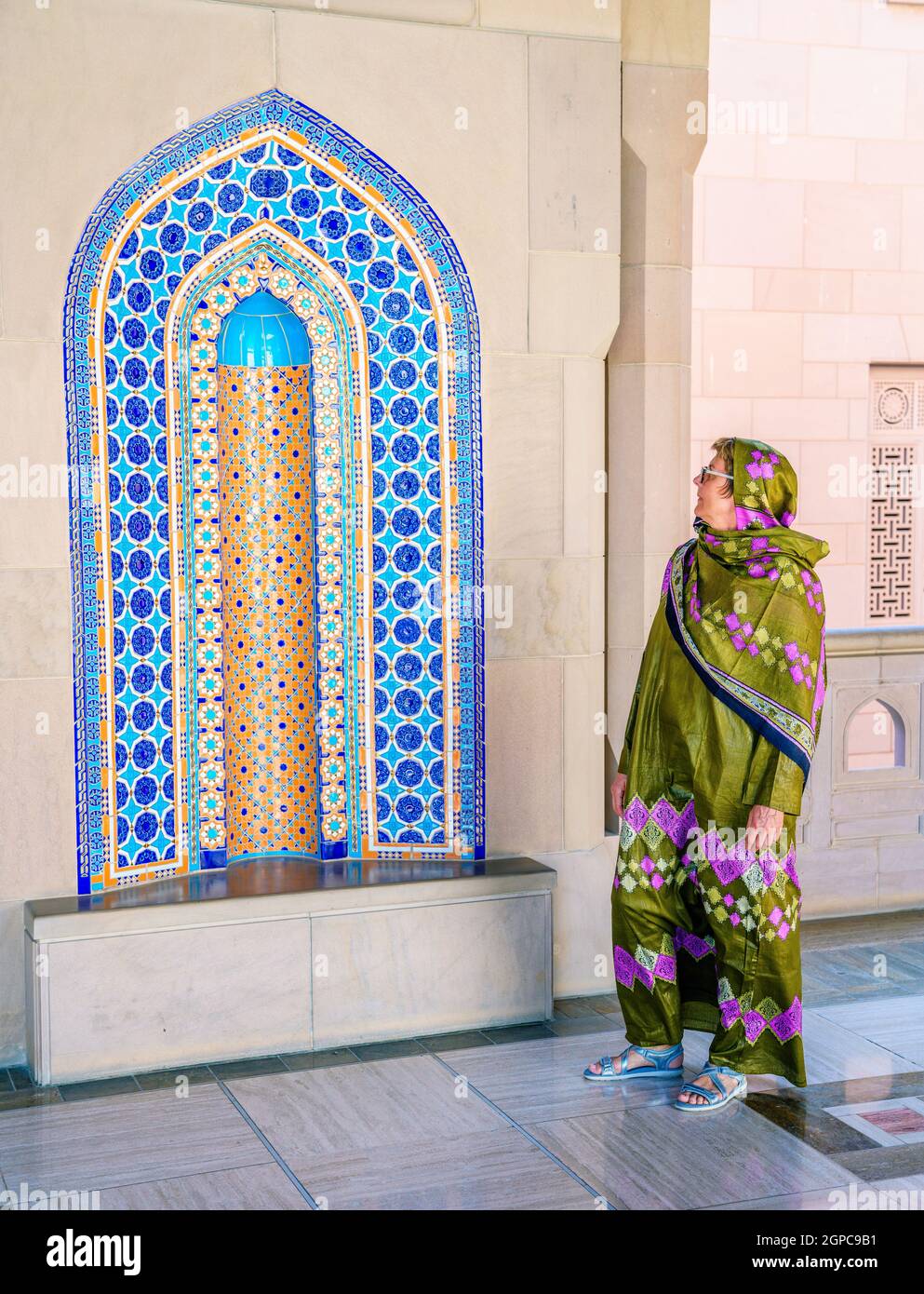 Eine Frau, die in einem traditionellen omanischen Abaya gekleidet ist und eine verzierte Nische in der Sultan Qaboos Moschee in Muscat, Oman, betrachtet Stockfoto