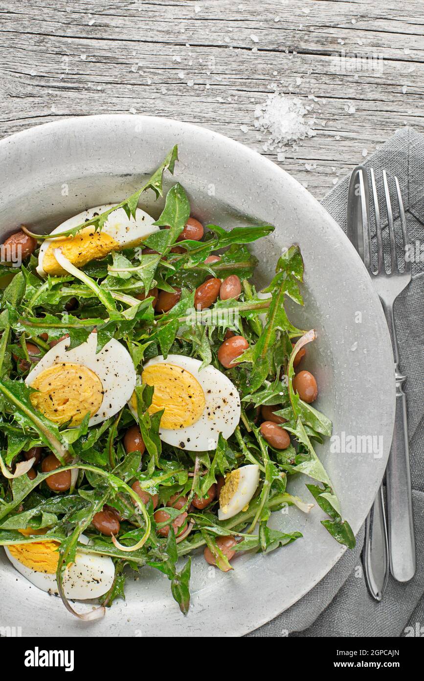 Frischer Löwenzahn-Salat mit Bohnen und Eiern auf Holzhintergrund Stockfoto