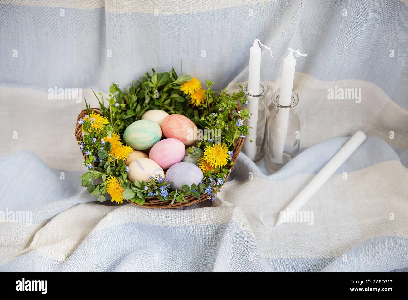 Ein schöner Frühlingsstrauß in einem Holzkorb mit Ostereiern, die mit Aquarellen bemalt sind. Weiße Kerzen liegen in der Nähe Stockfoto