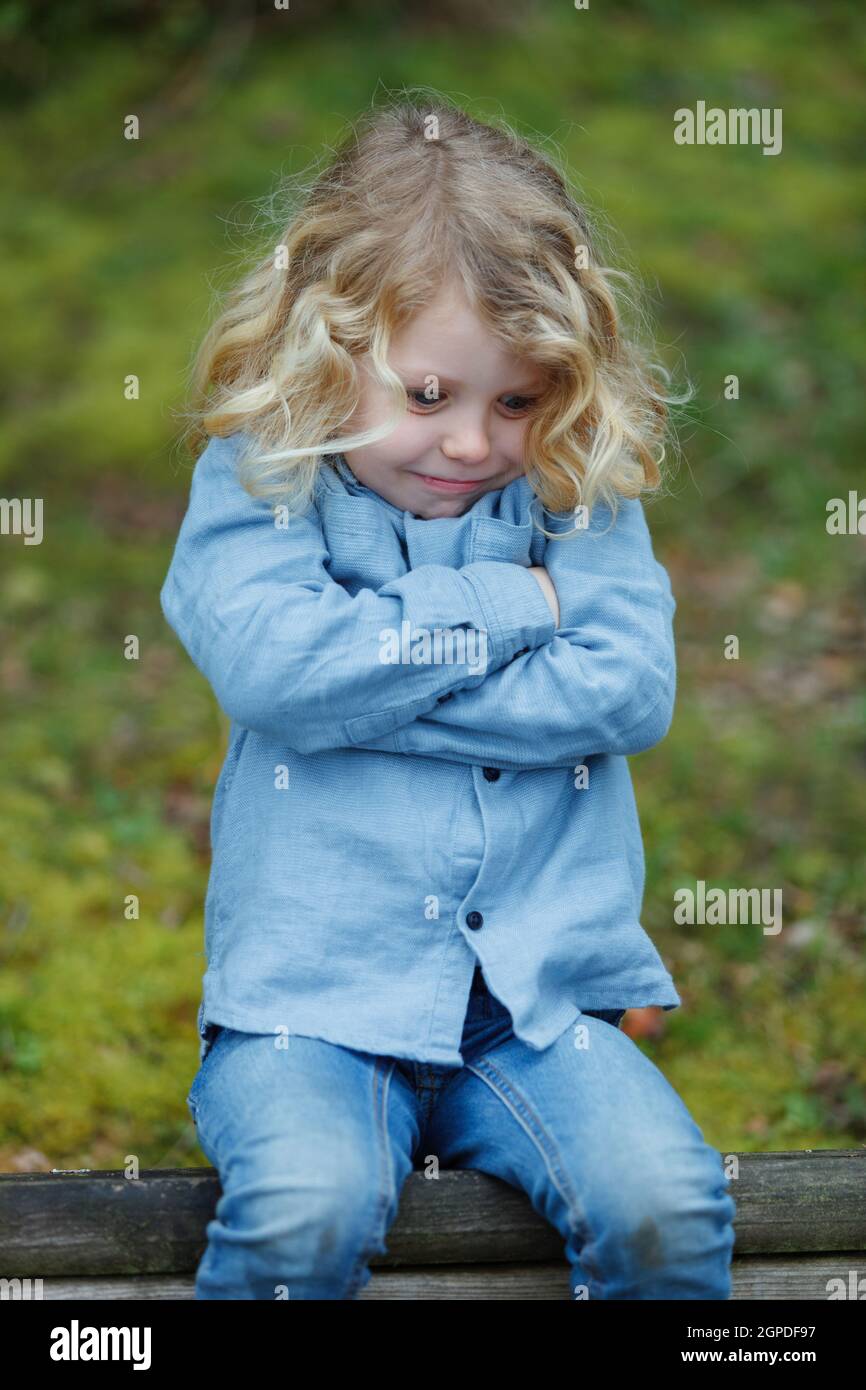 Wütend Kind mit langen blonden Haaren seine Arme auf einer Bank sitzen Kreuzung Stockfoto