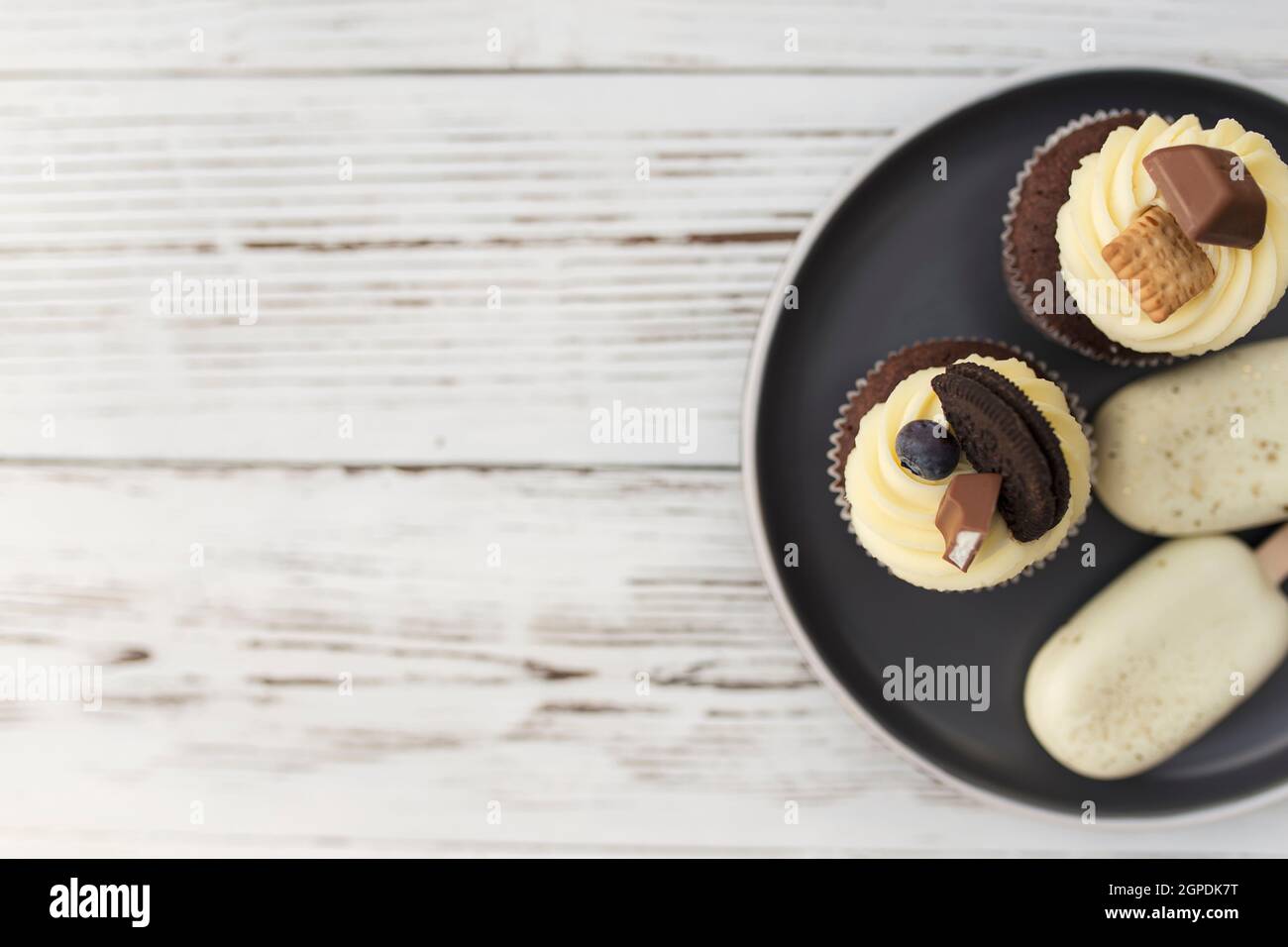 Weißes Plätzcheneis auf einem Stock und leckere Muffins und Cupcakes auf einem Tablett auf einem Holzhintergrund. Dekoriert mit verschiedenen Bonbons, Keksen und Colo Stockfoto