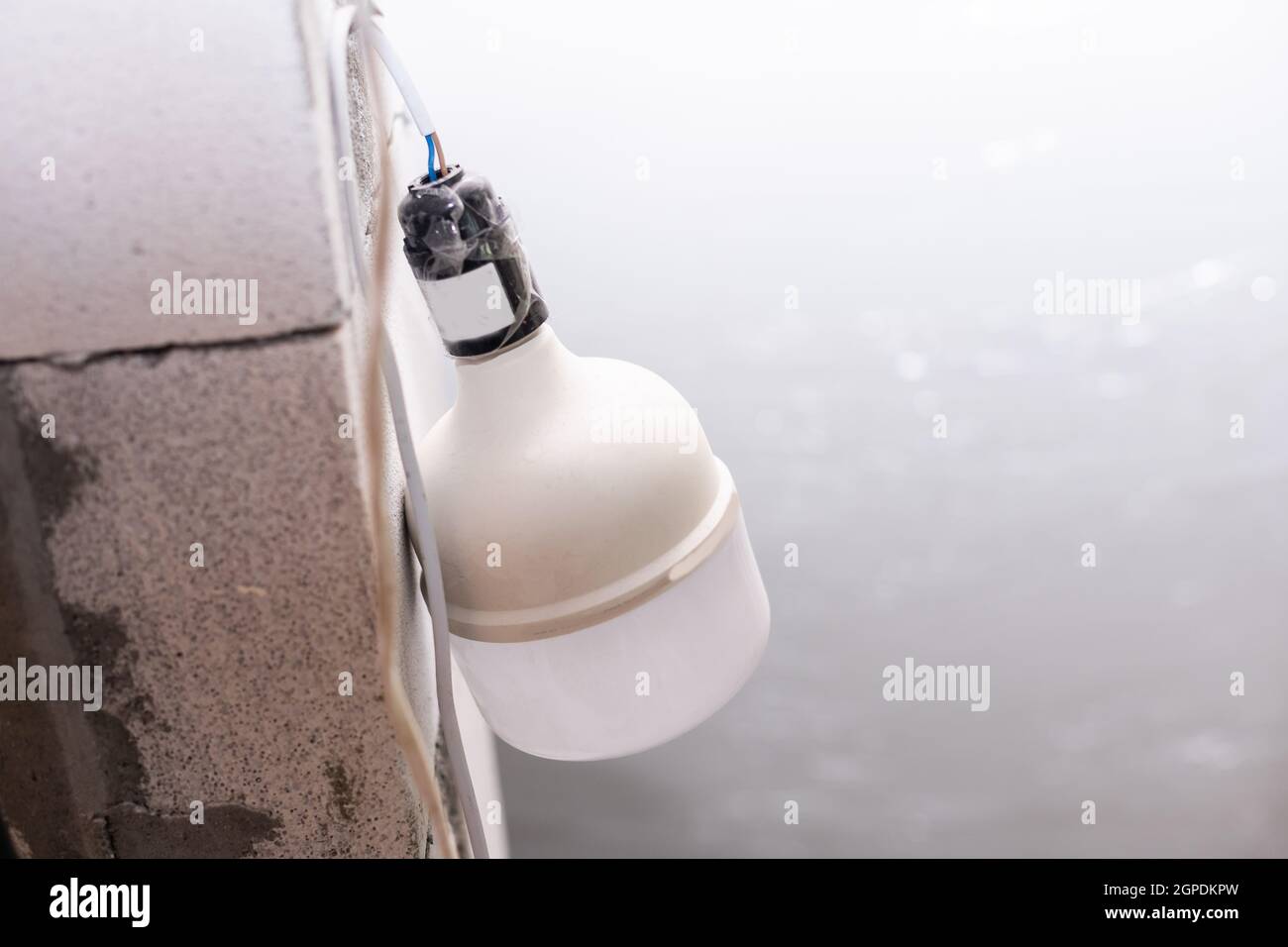 Große Lampe im leeren Kellerraum mit minimalen vorbereitenden Reparaturen im Inneren mit weißen Ziegelwänden Stockfoto