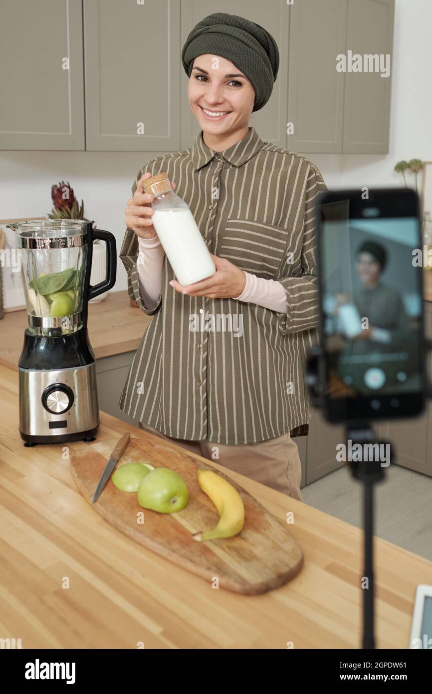 Vertikale mittellange Porträt der modernen muslimischen Frau in der Küche Kochen Smoothie vor der Kamera für Lebensmittel-Blog stehen Stockfoto