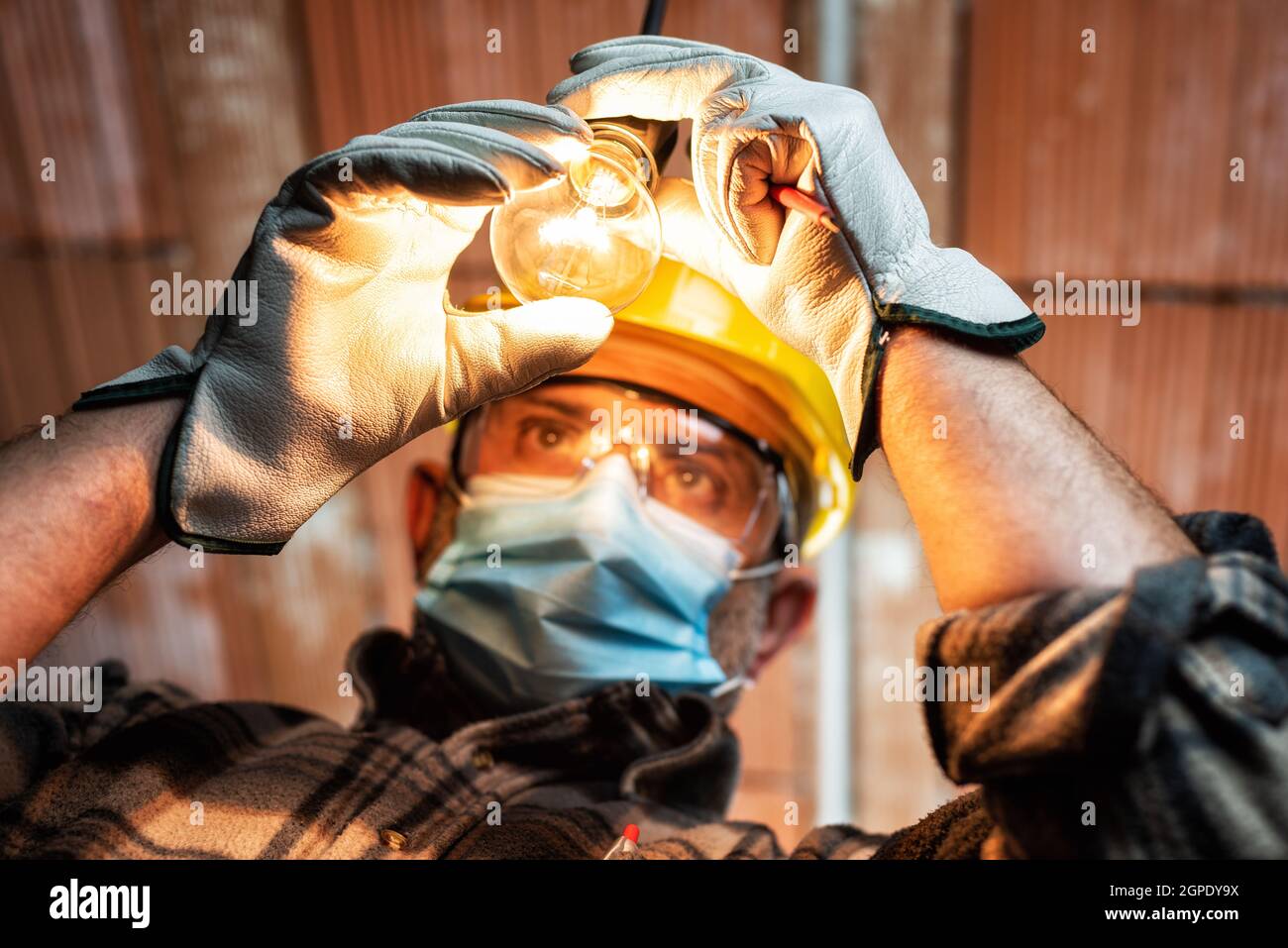 Elektriker bei der Arbeit ersetzt die Glühbirne durch Helm, Schutzbrille und Handschuhe geschützt. Tragen Sie die OP-Maske, um die Ausbreitung von COR zu verhindern Stockfoto