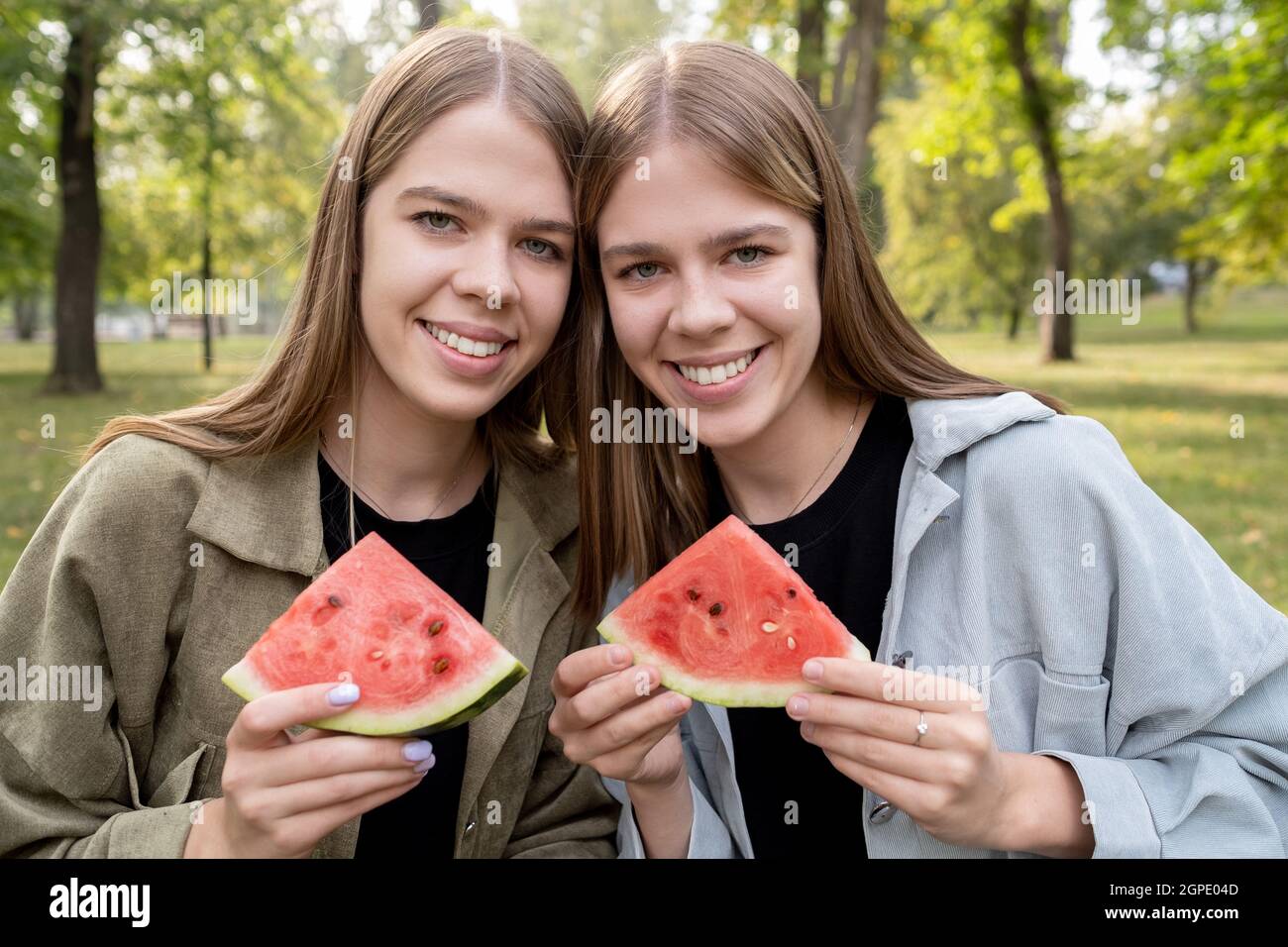 Zwei niedliche Mädchen mit Wassermelonenscheiben, die am Sommertag im Park ruhen Stockfoto