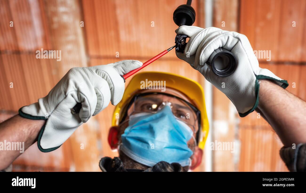 Elektriker Arbeiter bei der Arbeit ersetzt die Lampenfassung durch Helm, Schutzbrille und Handschuhe geschützt; tragen Sie die OP-Maske, um die Ausbreitung von Co zu verhindern Stockfoto