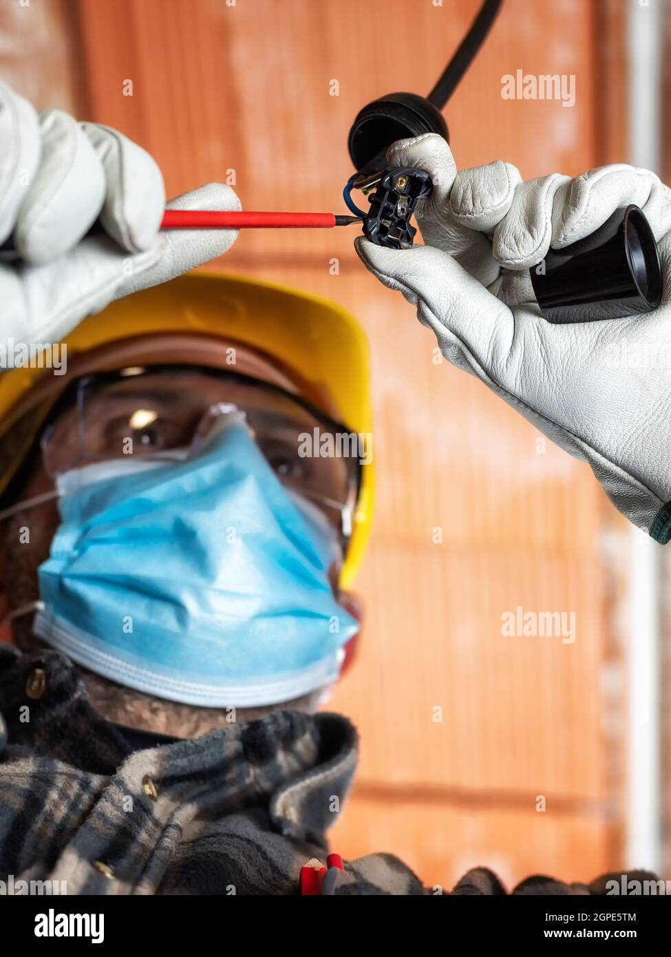 Elektriker Arbeiter bei der Arbeit ersetzt die Lampenfassung durch Helm, Schutzbrille und Handschuhe geschützt; tragen Sie die OP-Maske, um die Ausbreitung von Co zu verhindern Stockfoto