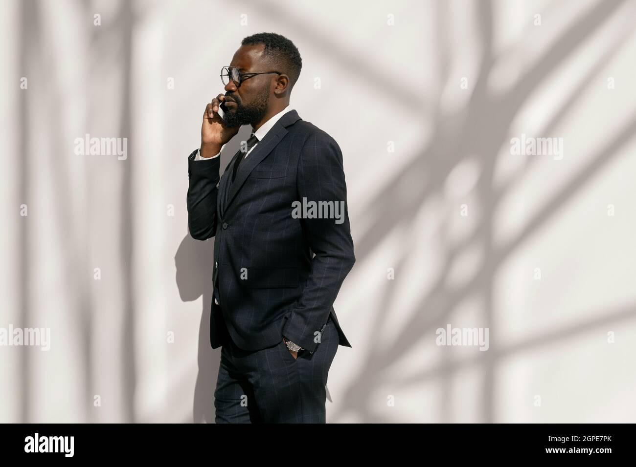 Seitenansicht eines ernsthaften Geschäftsmannes mit einem Smartphone am Ohr, das an einer weißen Wand steht Stockfoto