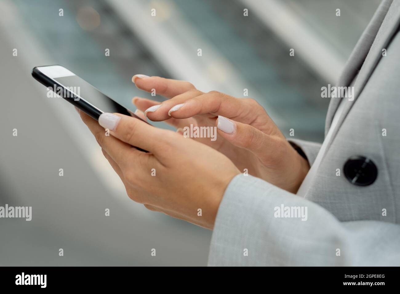 Hände der jungen Geschäftsfrau in grauer formalwear berühren Smartphone-Bildschirm Stockfoto