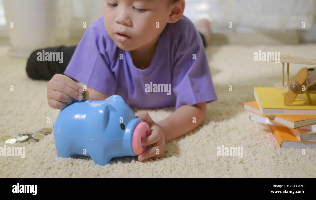 Glücklich asiatische Kind Junge Vorschule Putting Pin Geld Münzen in blau konfrontiert Ferkel slot. Kleines Kind Putting Münze in Sparschwein für das Sparen mit Haufen c Stockfoto