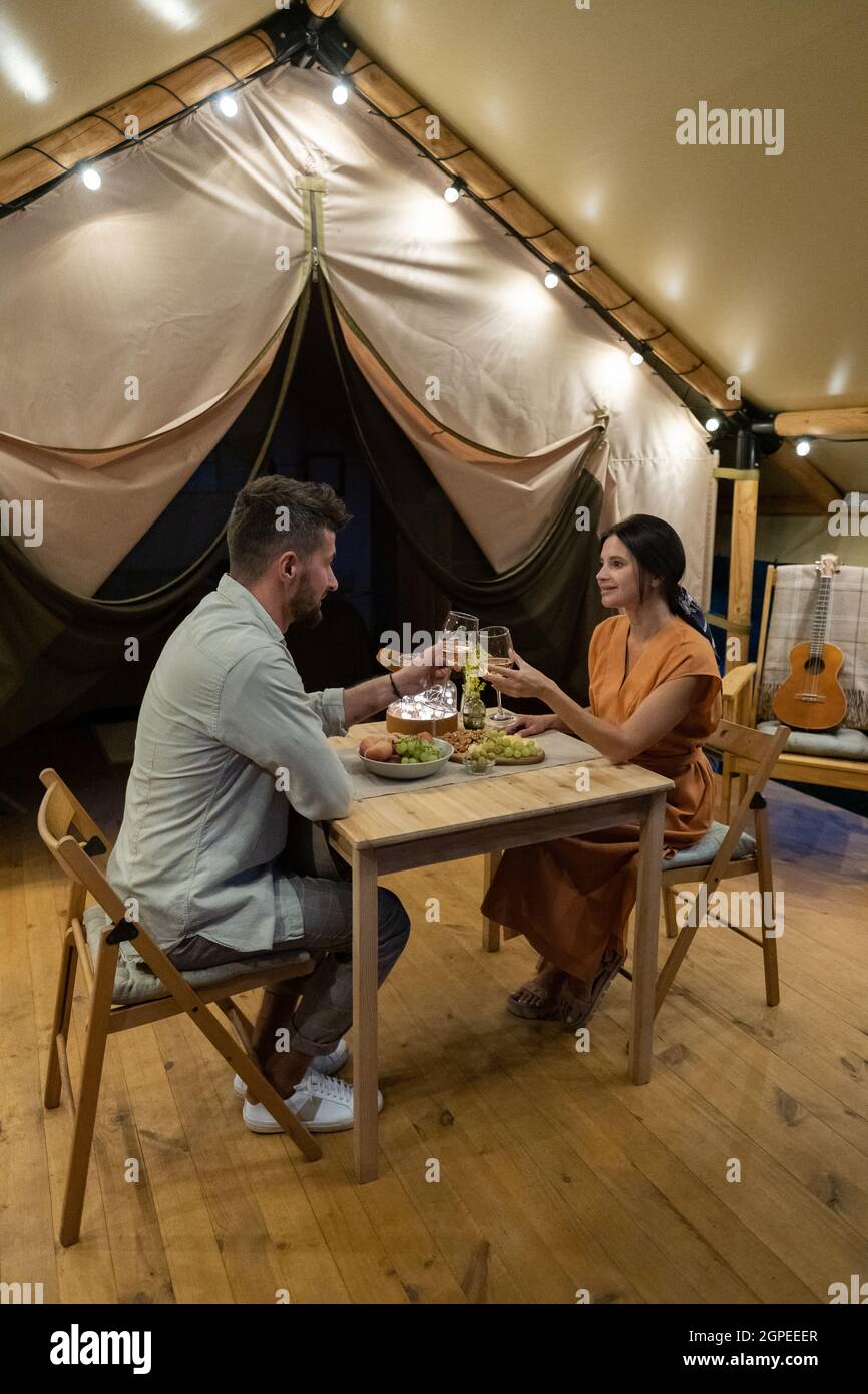 Ein junges, amoröses Paar, das auf der Terrasse des Glamping House mit einem Glas Wein über dem Tisch serviert wird Stockfoto