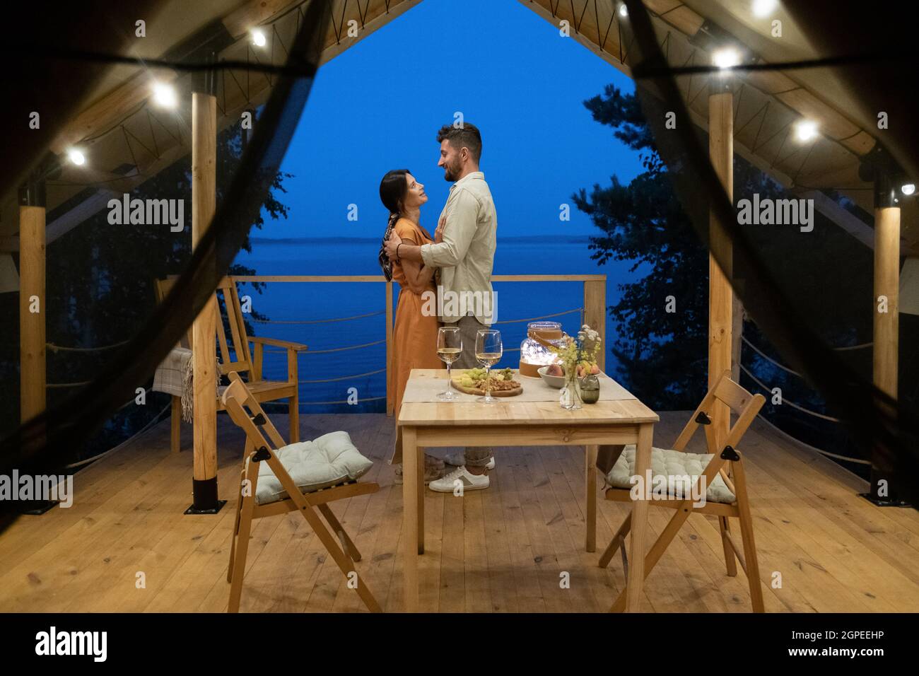 Junges Paar, das in Umarmung auf der Terrasse des Glamping-Hauses vor dem servierten Tisch steht Stockfoto