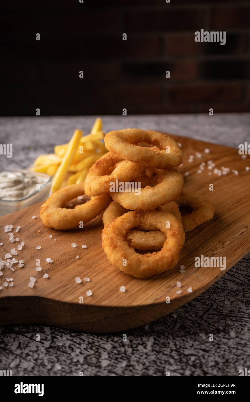 Selektiver Fokus. Gebratene Zwiebelringe in Semmelbröseln, in Öl gebraten. Mit natürlicher Sauce. Restaurant-Servieren. Auf dunklem Hintergrund. Für Menüs und Werbung Stockfoto