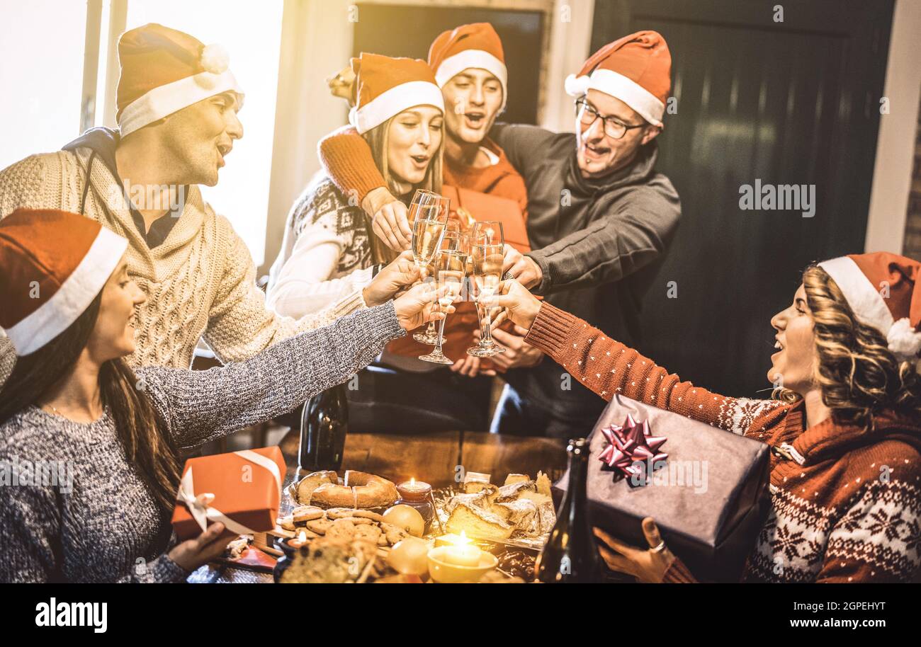 Freunde Gruppe mit santa Hüte Austausch Weihnachtsgeschenke mit Champagner Wein Toast zu Hause Abendessen - Winterurlaub Konzept mit jungen Menschen Stockfoto