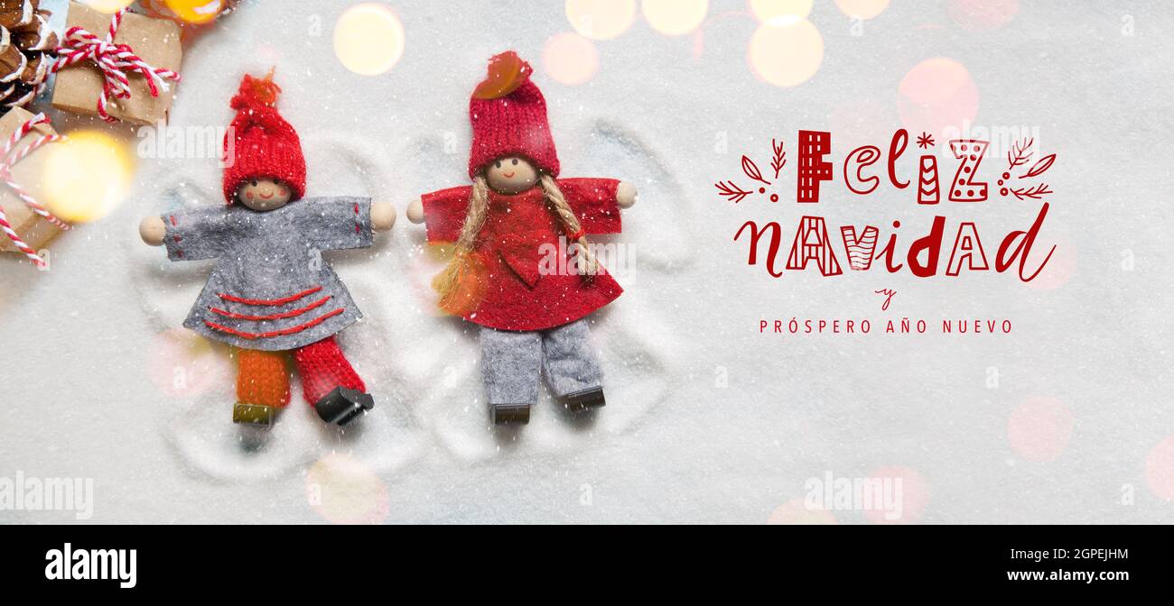 Weihnachtskarte mit kleinen Weihnachtspuppen Ornamente machen Engel im Schnee mit Lichtern Bokeh. Feliz Navidad lustige Handschrift-Schrift Stockfoto