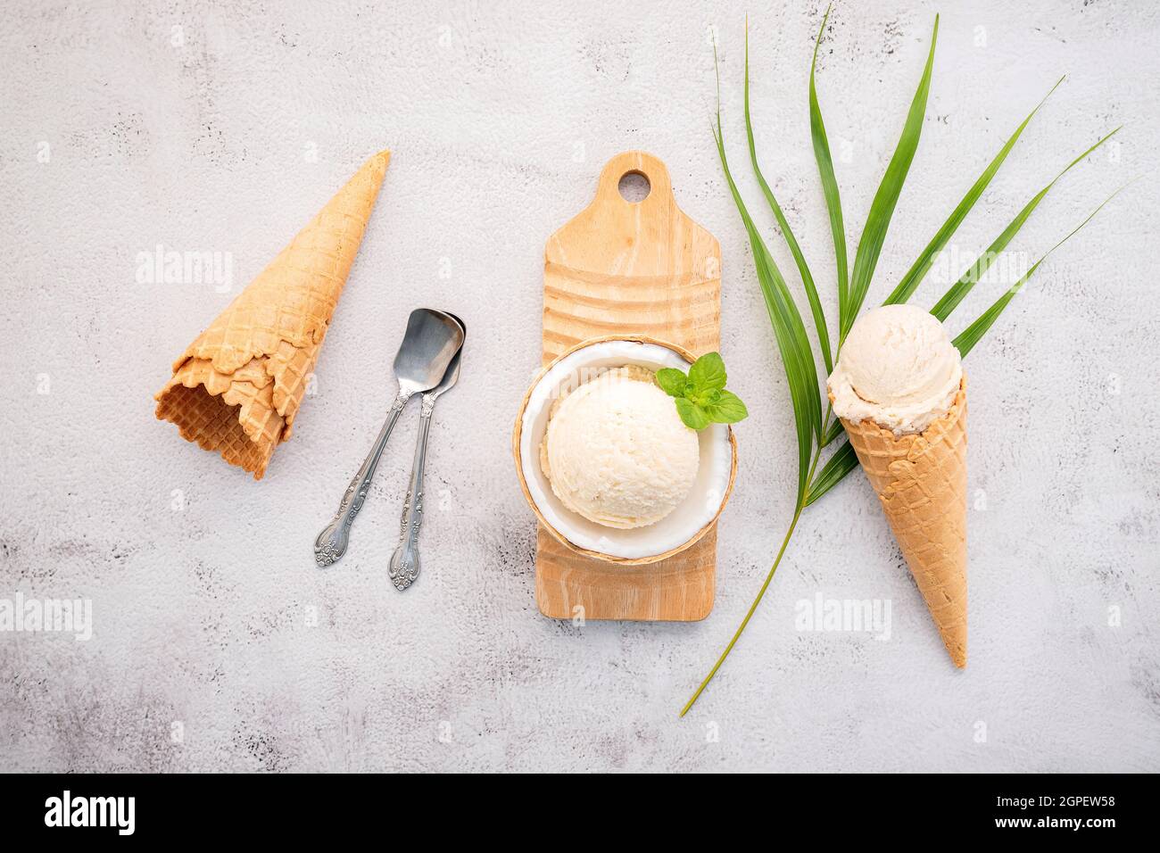 Kokoseis Aromen in der Hälfte der Kokosnuss Setup auf weißem Stein Hintergrund. Sommer und Süße Menükonzept. Stockfoto