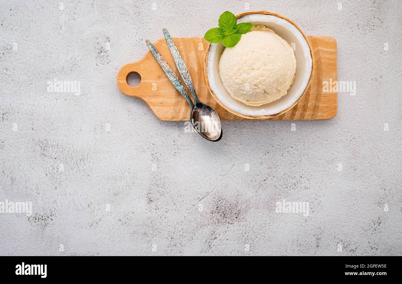 Kokoseis Aromen in der Hälfte der Kokosnuss Setup auf weißem Stein Hintergrund. Sommer und Süße Menükonzept. Stockfoto